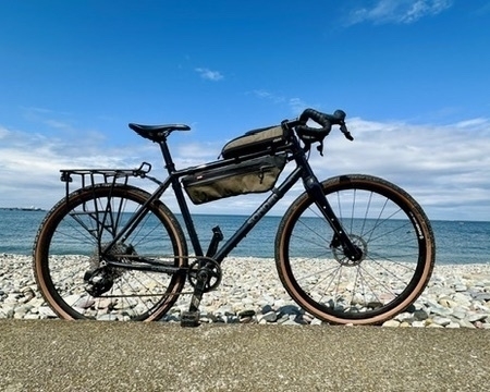 a gravel bike standing near a stone beach, looking out to the sea on a sunny day