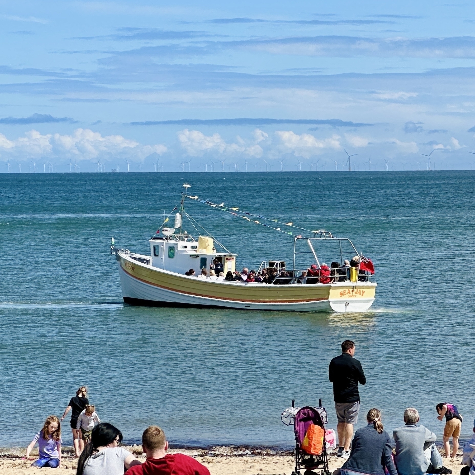 a small boat near the shore where tourists are sitting on sand 